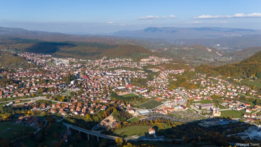 Panorama Mrkonjić Grada iz vazduha u jesen: grad u dolini, stadion, vijadukt i brda u jesenjim bojama