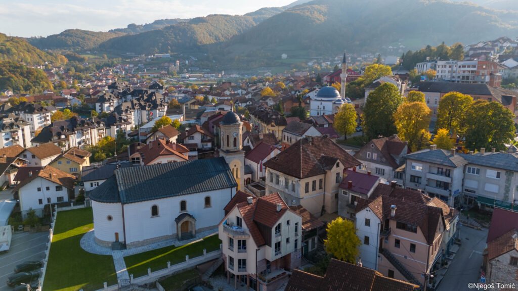 Centar Mrkonjić Grada iz vazduha u jesen: crkva sa zvonikom, crveni krovovi i žuto drveće